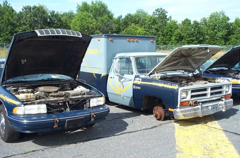 2001 Ford Crown Victoria - Two older vehicles, a sedan and a pickup truck, sit with their hoods open in an outdoor lot.