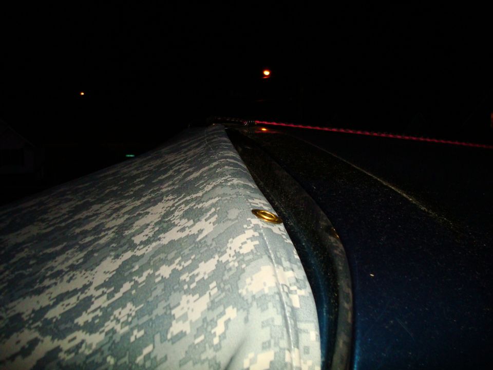 Camouflaged soft top on a dark blue vehicle at night. A red light streak is visible in the distance