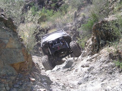1986 Toyota Hilux - This heavily modified off-road buggy tackles a challenging rocky incline in a desert environment.