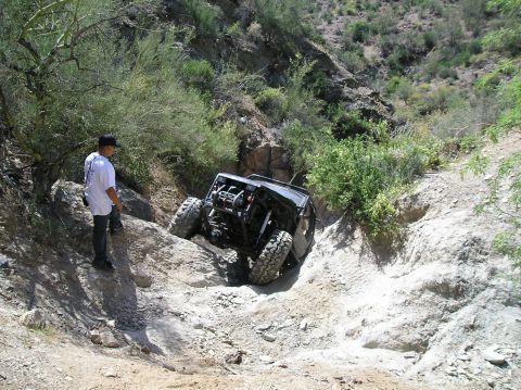 1986 Toyota Hilux - A person watches a heavily modified off-road vehicle descend a challenging rocky trail.