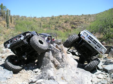 1986 Toyota Hilux - Two off-road vehicles navigate a challenging rocky terrain under a clear blue sky.