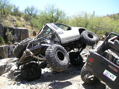 1986 Toyota Hilux - A heavily modified off-road vehicle navigates a challenging rocky trail, demonstrating extreme articulation and off-road capability.