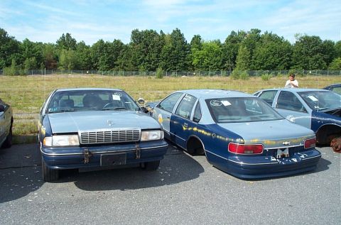 2001 Ford Crown Victoria - Two police sedans are parked side-by-side in an outdoor lot under a partly cloudy sky.