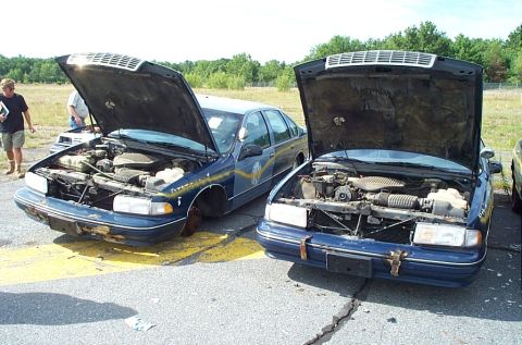 2001 Ford Crown Victoria - Two older model sedans, likely from the 1990s, are parked with their hoods open, revealing their engines.