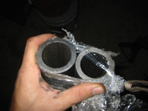 1995 Ford Bronco - Two exhaust pipes are held in a hand, wrapped in clear plastic packaging.