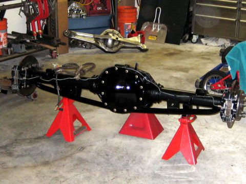 1996 Ford Bronco - A black rear axle assembly is supported by red jack stands in a garage setting.
