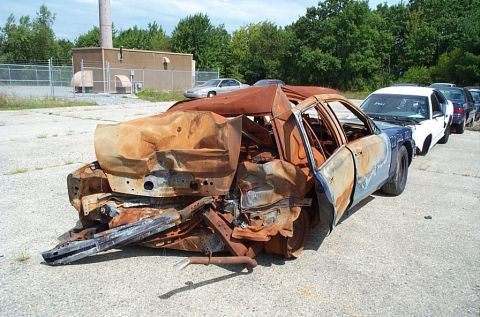 2001 Ford Crown Victoria - A severely damaged and burnt vehicle sits in a lot, with other cars lined up behind it.