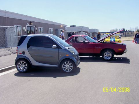1972 Ford Ranchero - Two cars, a red AMC Gremlin X and a silver Smart car, are parked outside a building on a sunny day.