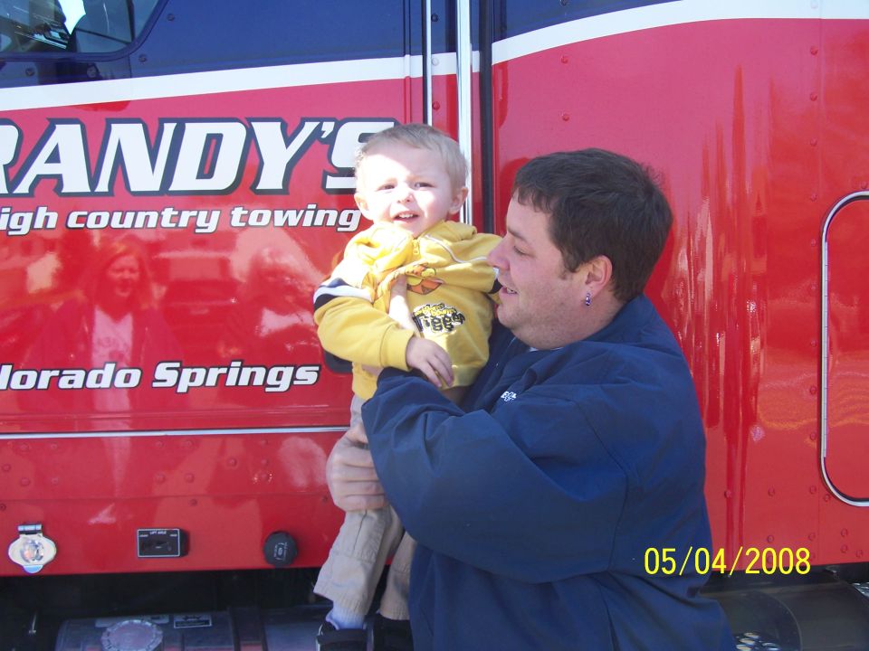 Man holding child in front of red "Randy's High Country Towing" truck