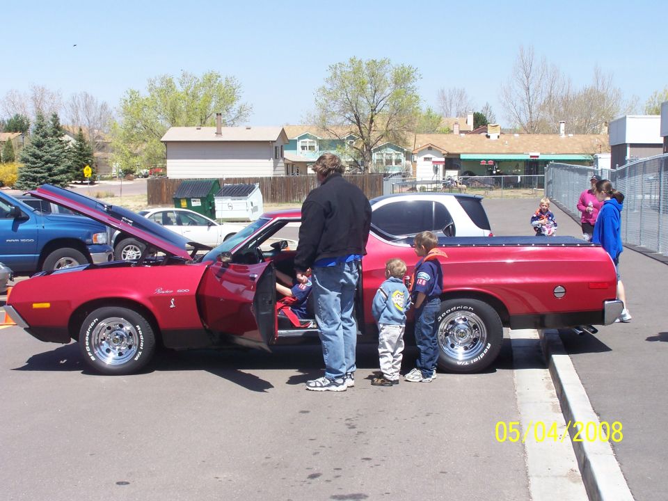 Red 1972 Ford Ranchero with open hood and door, side view, people gathered around
