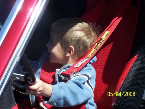 1972 Ford Ranchero - A young child is seated in a red racing seat with a harness, holding onto a steering wheel.