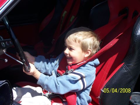 1972 Ford Ranchero - A young boy smiles while holding the steering wheel inside a vehicle with racing seats and harnesses.