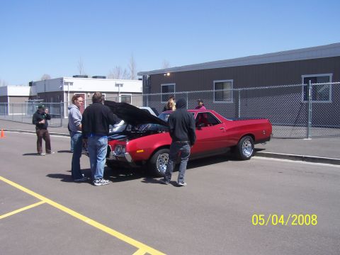 1972 Ford Ranchero - A group of people are gathered around a red coupe utility vehicle with its hood open on a sunny day.