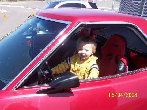1972 Ford Ranchero - A young child sits behind the steering wheel of a red vehicle with racing seats.