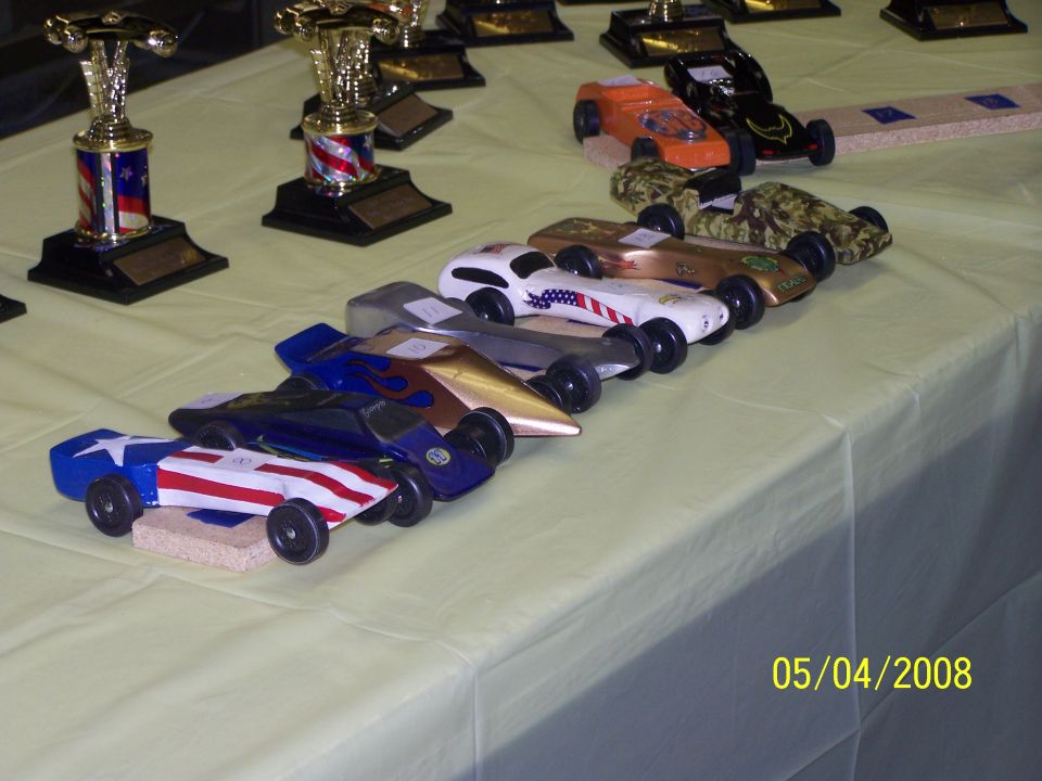 Pinewood derby cars with patriotic and camouflage paint schemes, lined up for a race