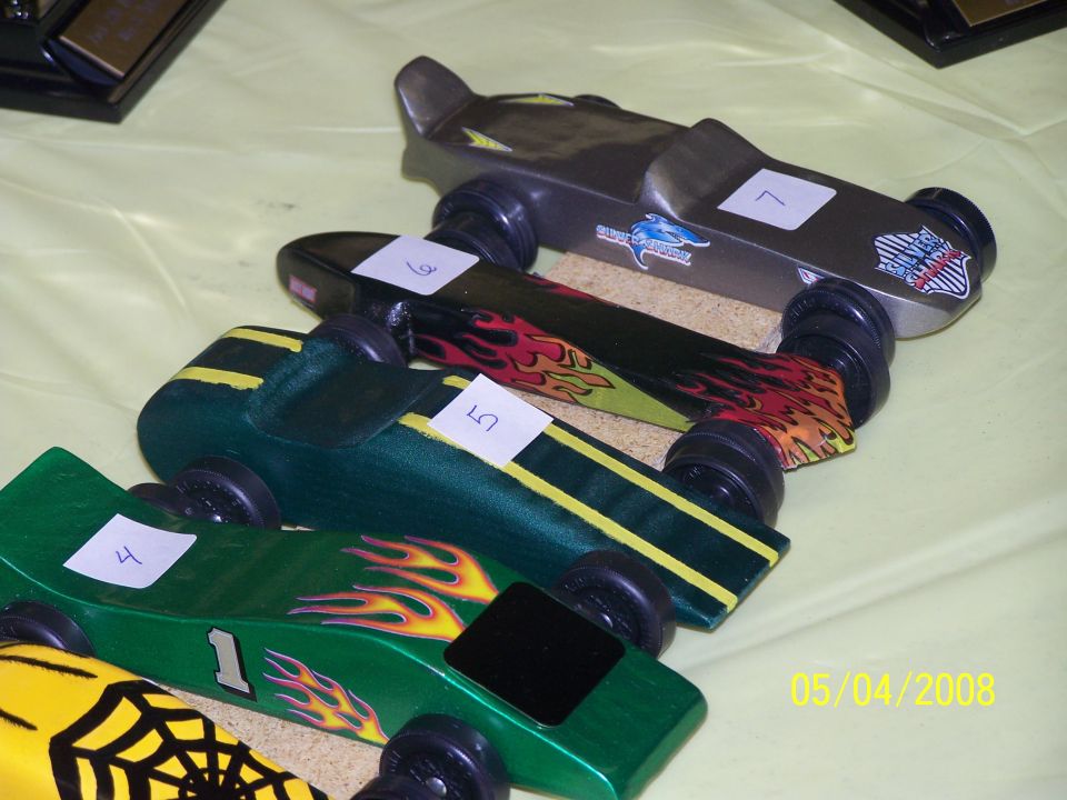 Several pinewood derby cars lined up, some with flame decals and numbers