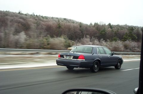2001 Ford Crown Victoria - dark blue Ford Crown Victoria sedan travels a highway alongside bare wintry trees, shot from a following vehicle.