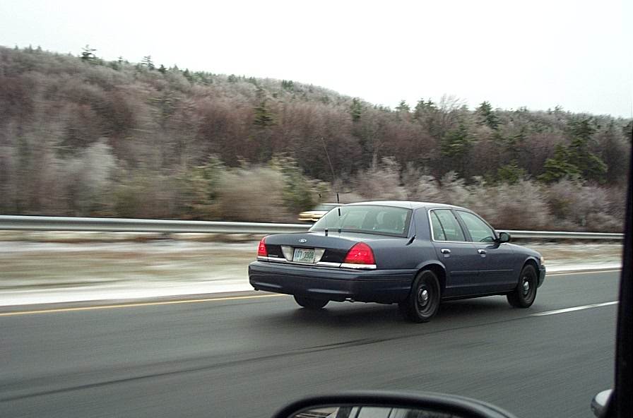 Dark blue Ford Crown Victoria sedan driving on a highway past wintry hills