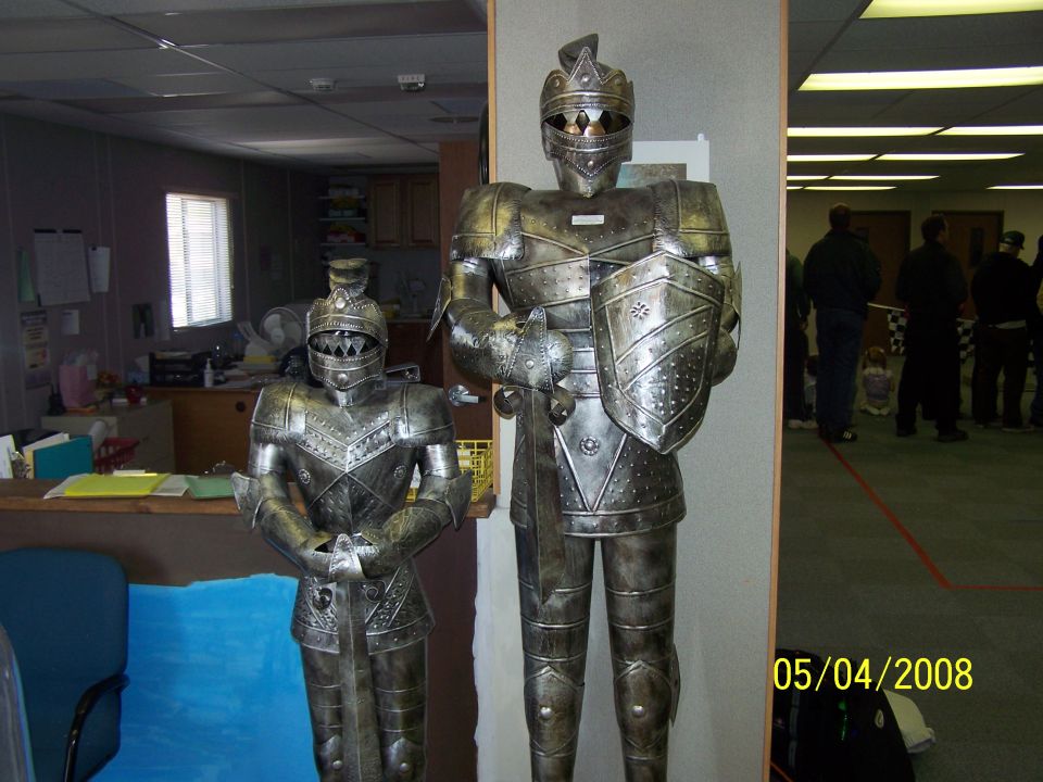 Two metal suits of armor stand in an office, one smaller than the other