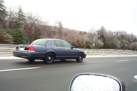 2001 Ford Crown Victoria - Rolling 3/4 rear shot of a dark blue Ford Crown Victoria sedan on a highway, taken from another moving vehicle with the photographer's mirr…