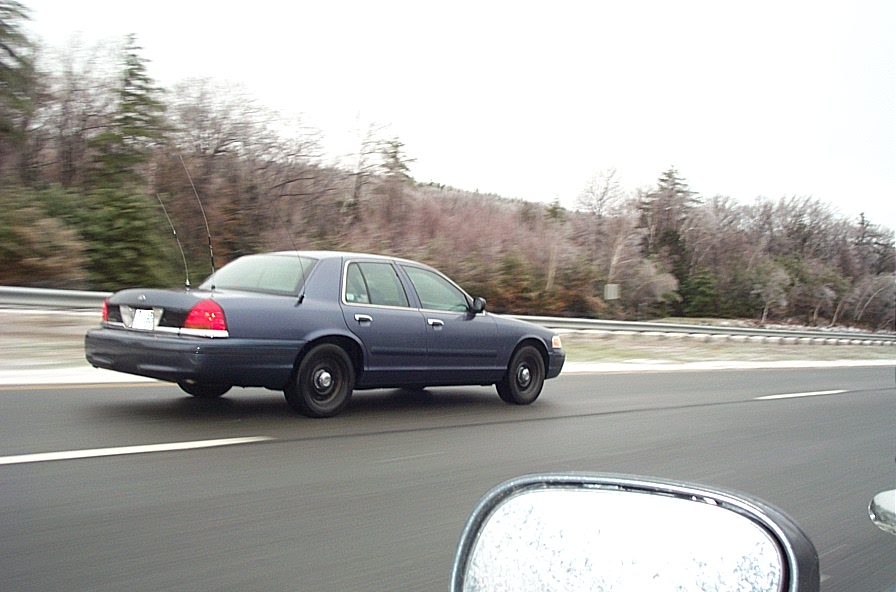 Dark blue unmarked Crown Victoria sedan with steel wheels and trunk antennas on highway