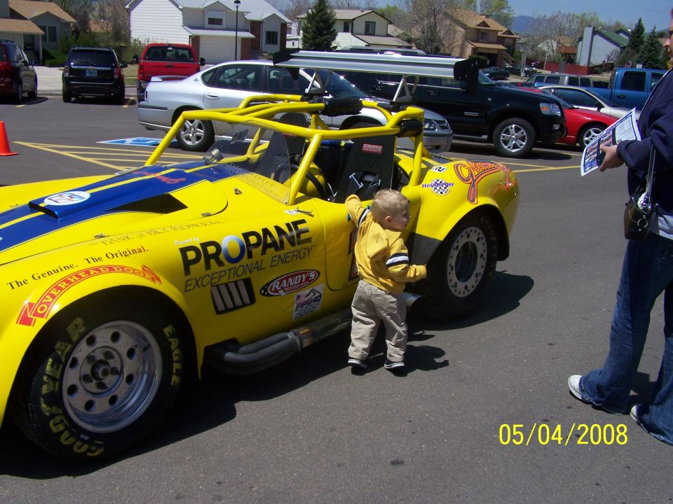 Yellow custom race car with blue stripes, 'PROPANE EXCEPTIONAL ENERGY' text, and a child looking at the wheel