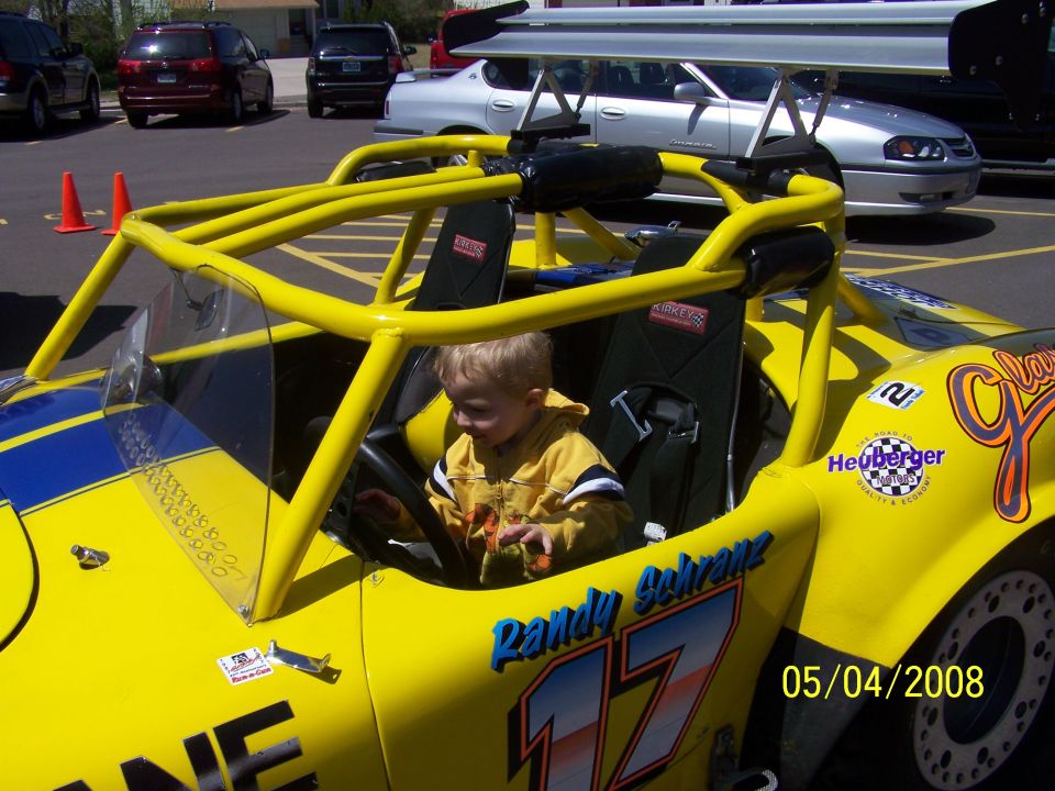 Yellow go-kart with blue stripes, roll cage, and racing decals. A young child is in the driver's seat