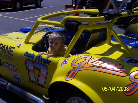 1972 Ford Ranchero - A young child sits in the driver's seat of a bright yellow, open-cockpit race car, ready for the track.