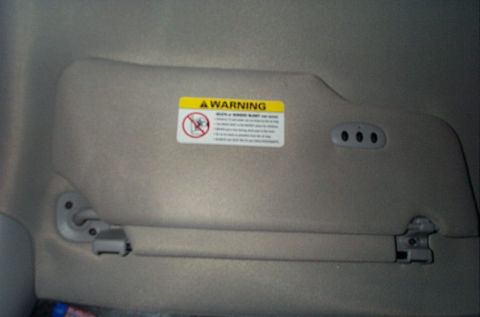 2001 Ford Crown Victoria - Interior shot of a car's sun visor with a warning label and garage door opener buttons.