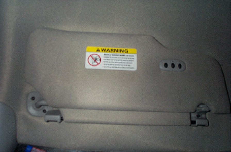 Sun visor with a warning sticker and three buttons for garage door opener