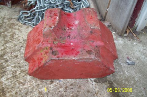 1900 Ford Wagon - A red metal block, possibly a counterweight or part, sits on concrete next to a heavy chain.