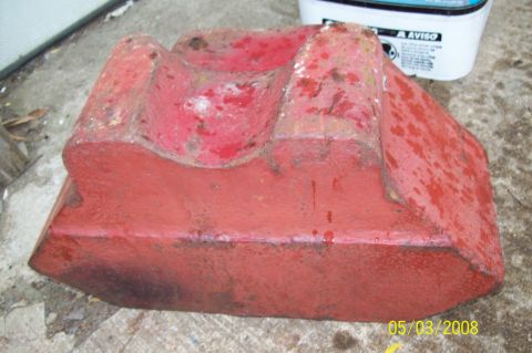 1900 Ford Wagon - A red metal object with a curved top rests on a concrete surface.