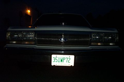 2001 Ford Crown Victoria - The front grille and headlights of a 2001 Ford Crown Victoria are visible at night, illuminated by its license plate light.