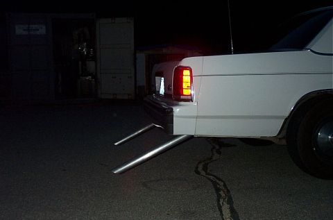 2001 Ford Crown Victoria - White sedan with custom dual exhaust pipes visible at night.