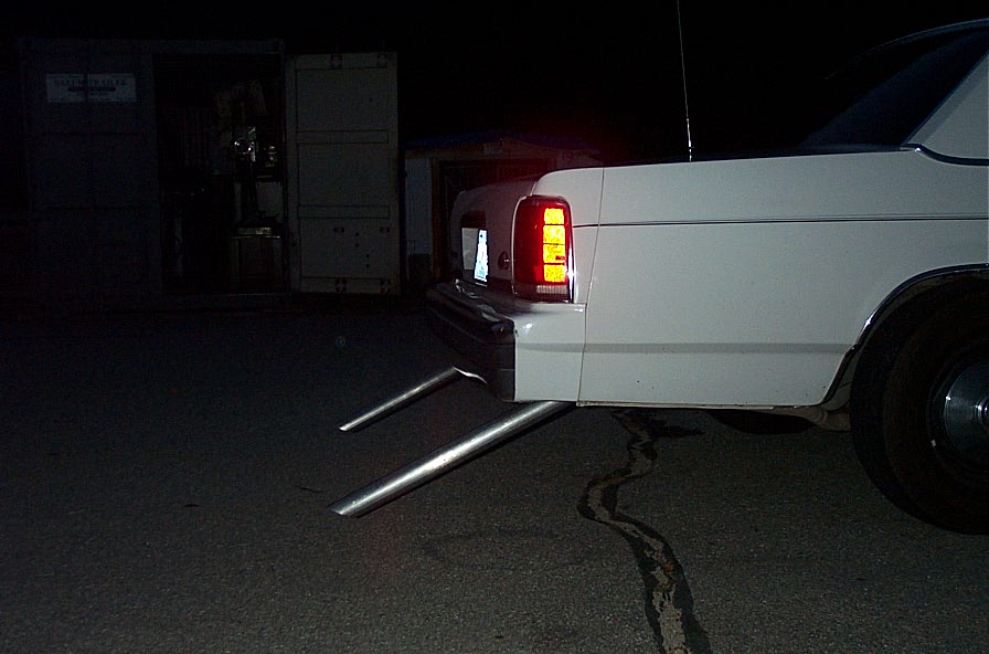 Rear quarter panel and taillight of a white sedan with large chrome exhaust pipes exiting the bumper