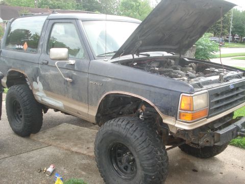 1989 Ford Bronco II - A dark blue 1989 Ford Bronco II with its hood open and modified suspension sits in a driveway.