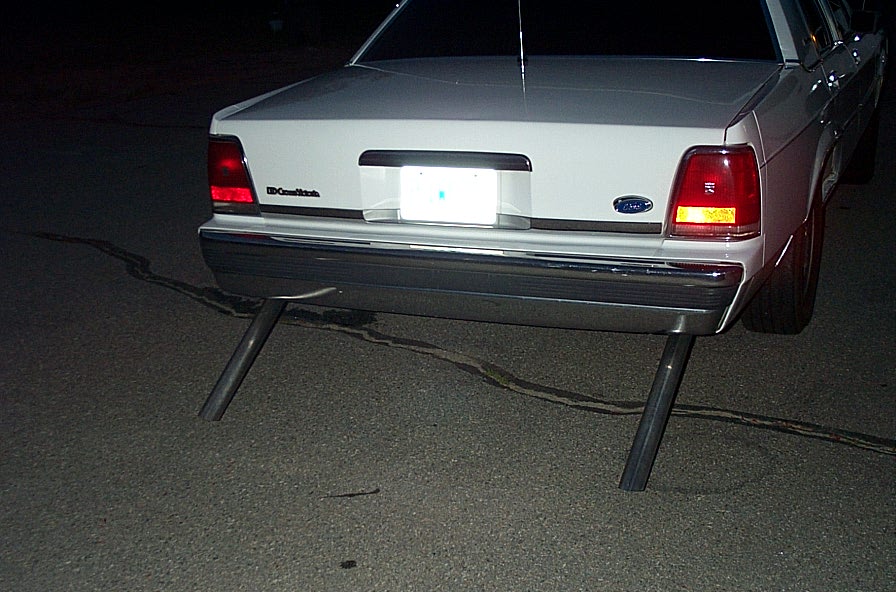 Rear of white Ford Crown Victoria at night with dual straight pipes below the bumper