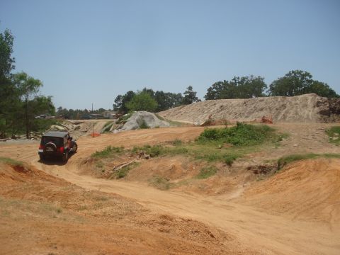 1989 Ford Bronco II - A red Jeep navigates a dirt path through a construction site with large piles of dirt and sand.