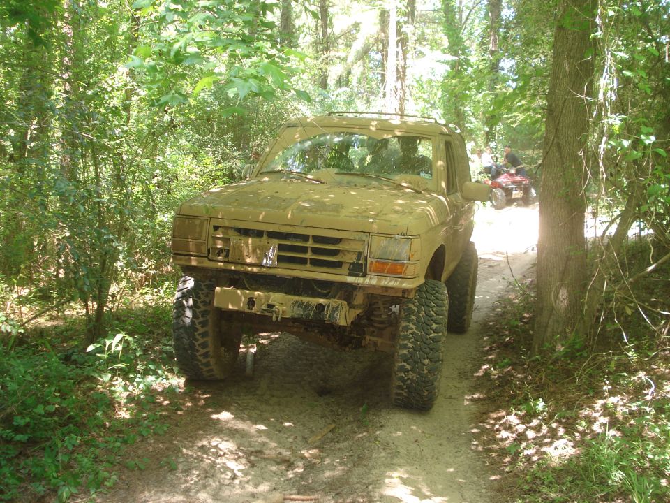 Mud-covered 1989 Ford Bronco II on a wooded trail with an ATV in the background