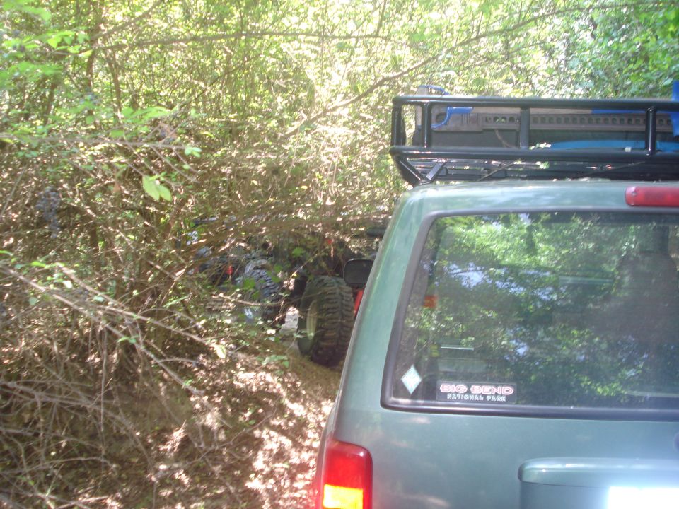 Green SUV with roof rack on a trail, another off-road vehicle visible in the trees