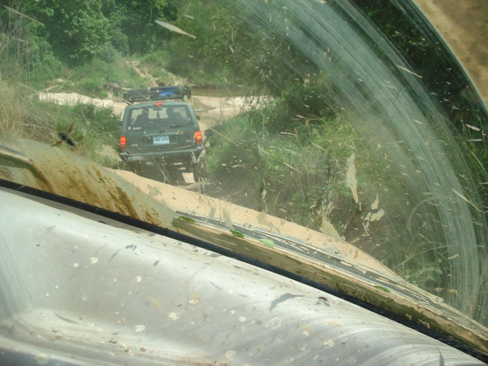 Mud-splattered 1989 Ford Bronco II driving on a dirt road, seen from inside another vehicle