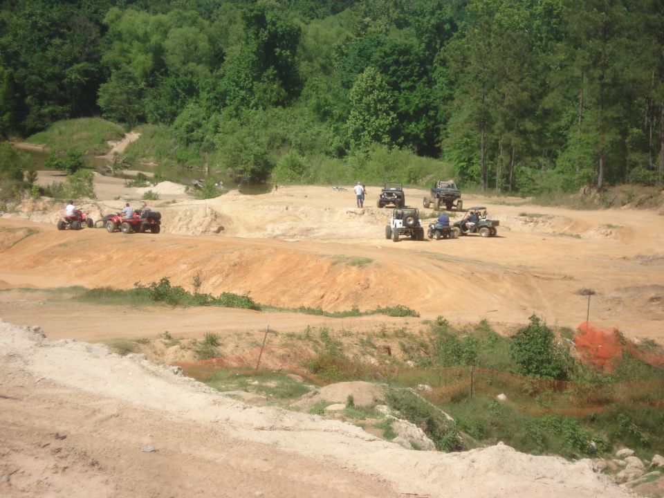 Several ATVs and off-road vehicles gathered on a dirt track with wooded hills in the background
