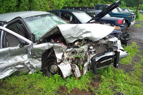 2001 Ford Crown Victoria - A severely damaged 2001 Ford Crown Victoria sits on a grassy area, with other vehicles visible in the background.
