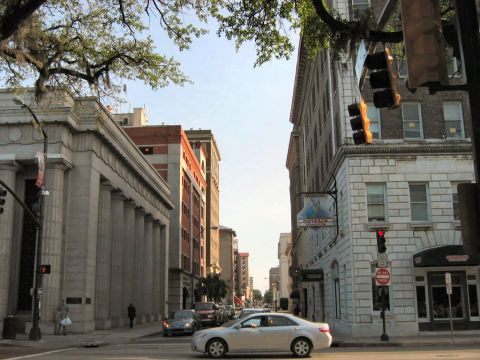 1985 Ford LTD Crown Victoria - Downtown street scene of a historic Southern city, looking down an avenue lined with a columned stone bank building, brick and stucco store…