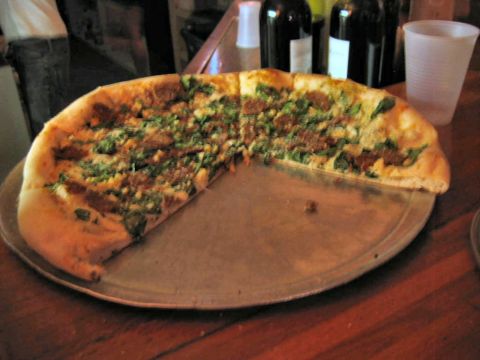 1985 Ford LTD Crown Victoria - A pizza with green toppings sits on a metal tray, with bottles and a cup visible in the background.