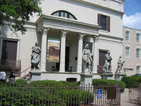 1985 Ford LTD Crown Victoria - A building with classical architecture features statues and banners, with greenery in the foreground.