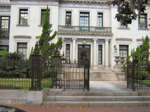 1985 Ford LTD Crown Victoria - A grand white building with a prominent entrance and decorative iron fencing is seen from the street.