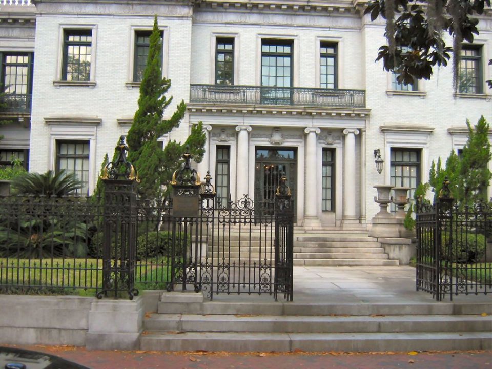 ornate black iron gate in front of a large white building with columns and many windows