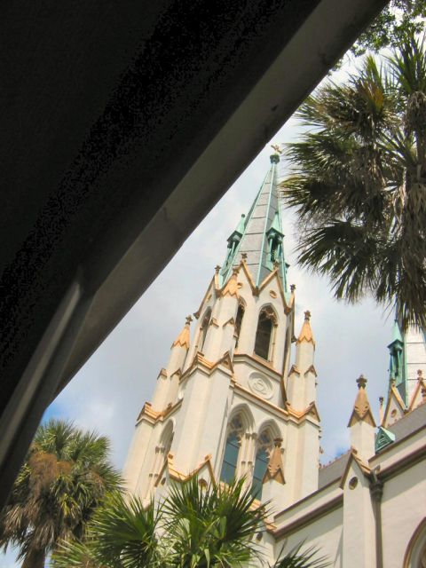 1985 Ford LTD Crown Victoria - A tall church steeple with gothic architectural elements is partially obscured by palm trees and an overhead structure.
