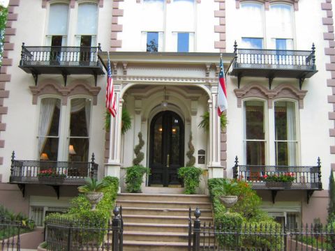 1985 Ford LTD Crown Victoria - A stately home entrance features a wide staircase leading to a dark arched doorway, flanked by American and Georgia flags.